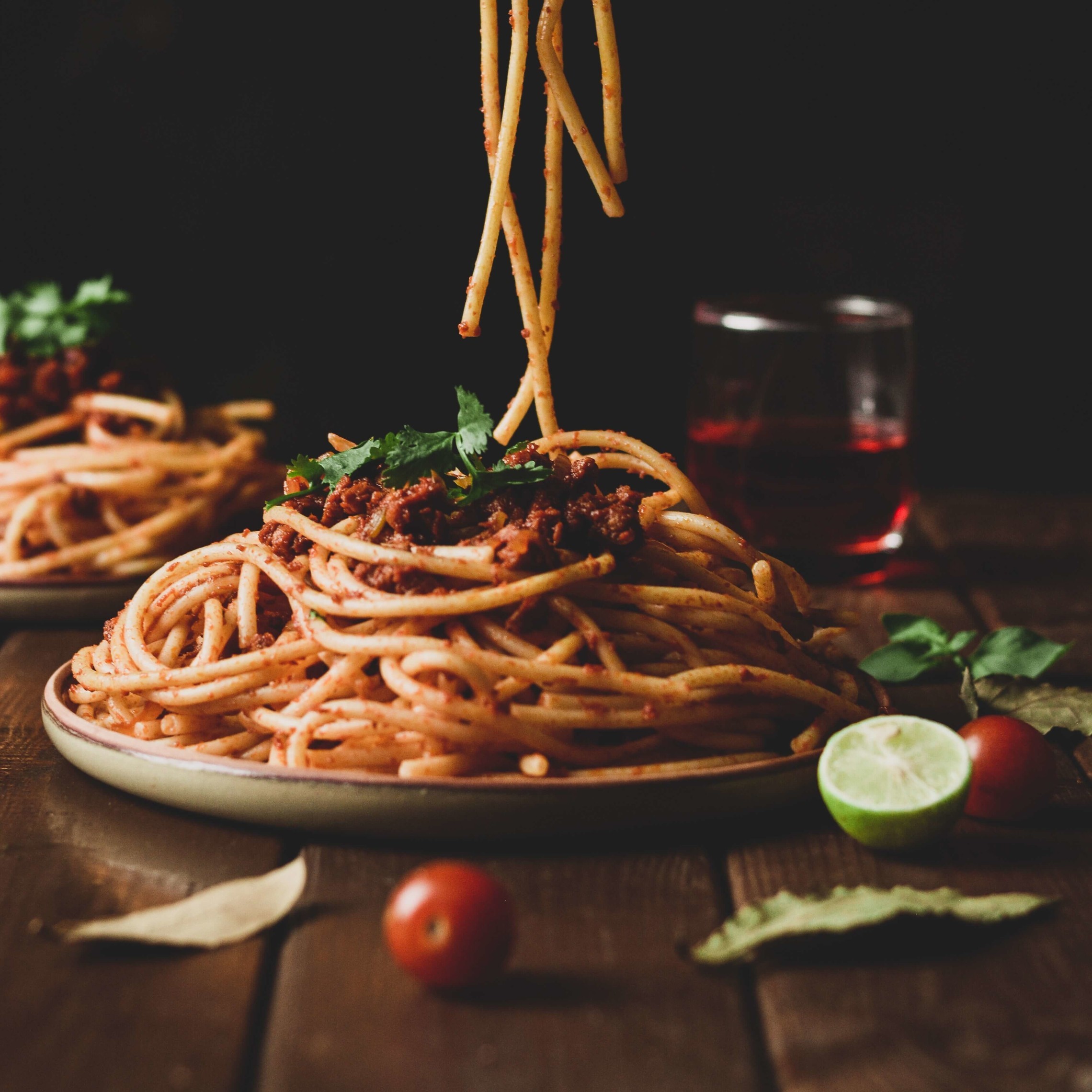 a plate of spaghetti with tomato sauce sits on a wooden table with an unseen person grabbing a forkfull of noodles