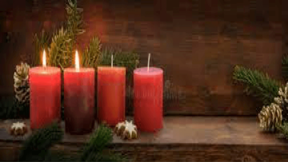 Four Advent Candles sit on a wooden bench with pinecones and garland. Two candles are lit. 