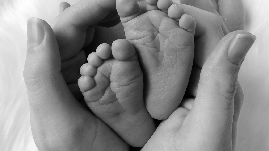 black and white photo of baby feet surrounded by two adult hands