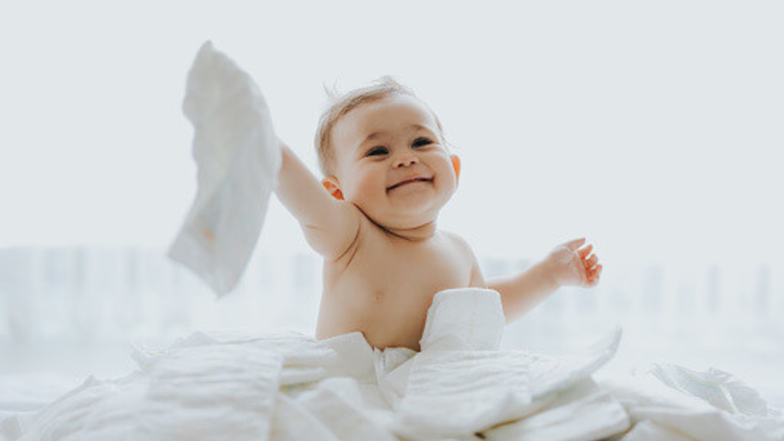 photo of small baby playing in a pile of new diapers