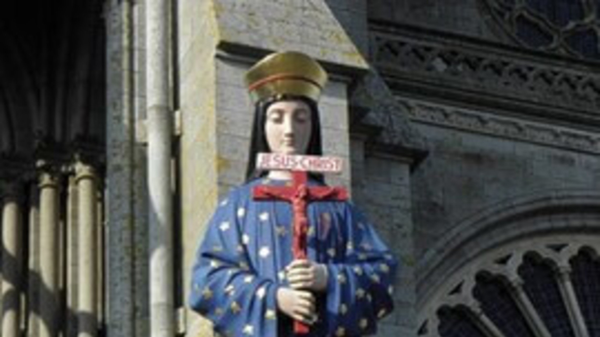 a statue of the Marian apparition in Pontmain holds a red crucifix 