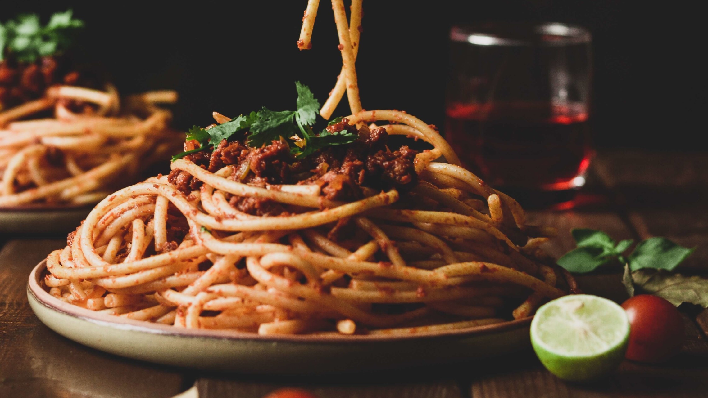 a plate of spaghetti with tomato sauce sits on a wooden table with an unseen person grabbing a forkfull of noodles