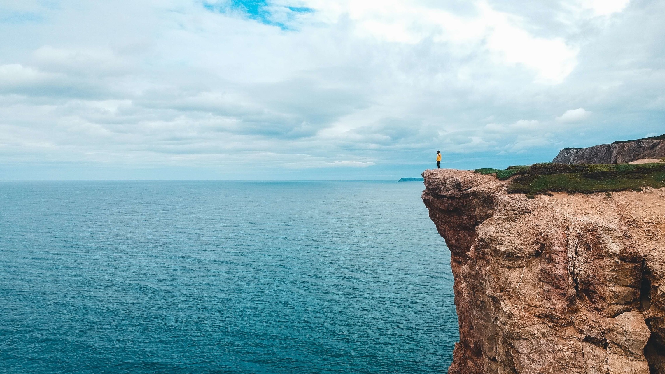 landscape photo of a rockface cliff overlooking the ocean with a solitary person at the edge