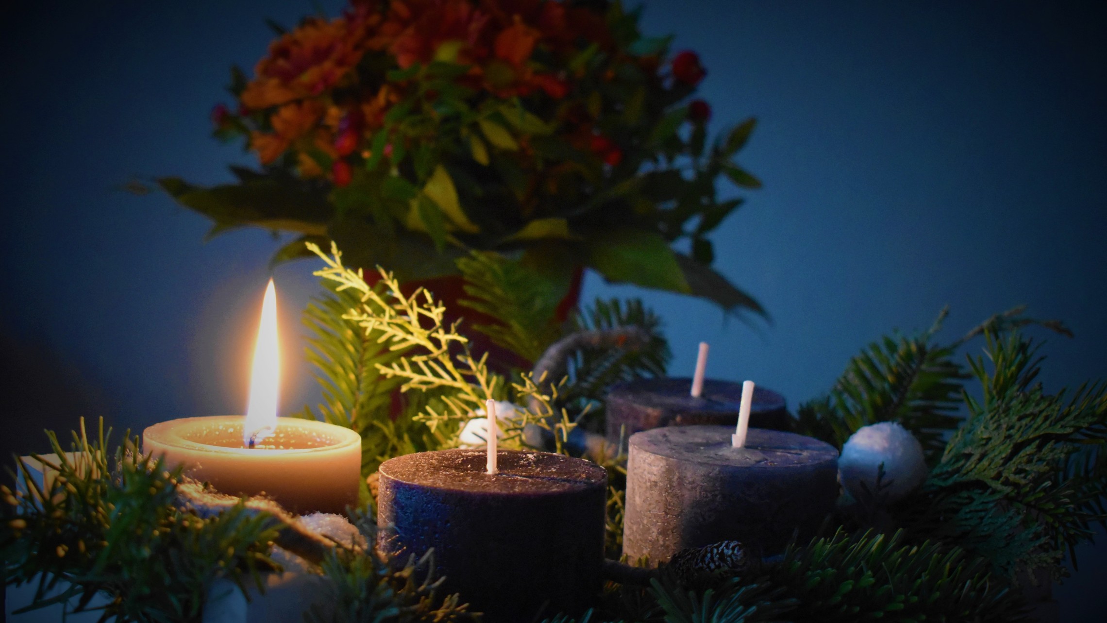 one lit candle, three unlit candles among some ferns