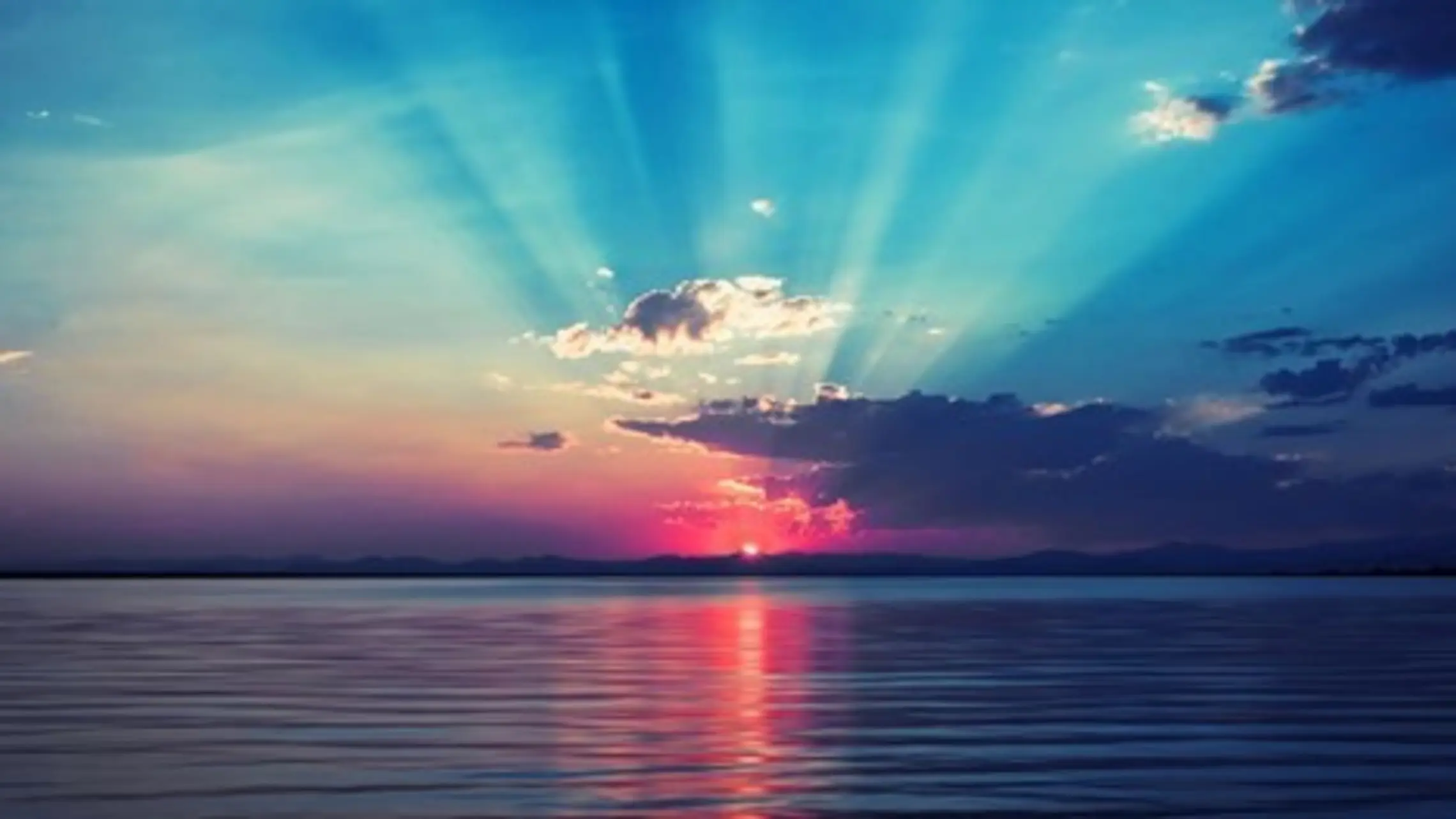 hues of blue, pink, gold and red line a calm sea. the sun goes down. 