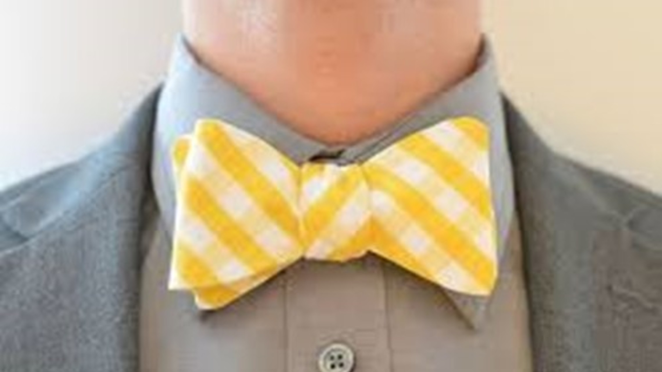 a man in a gray suit wears a yellow checked bow tie