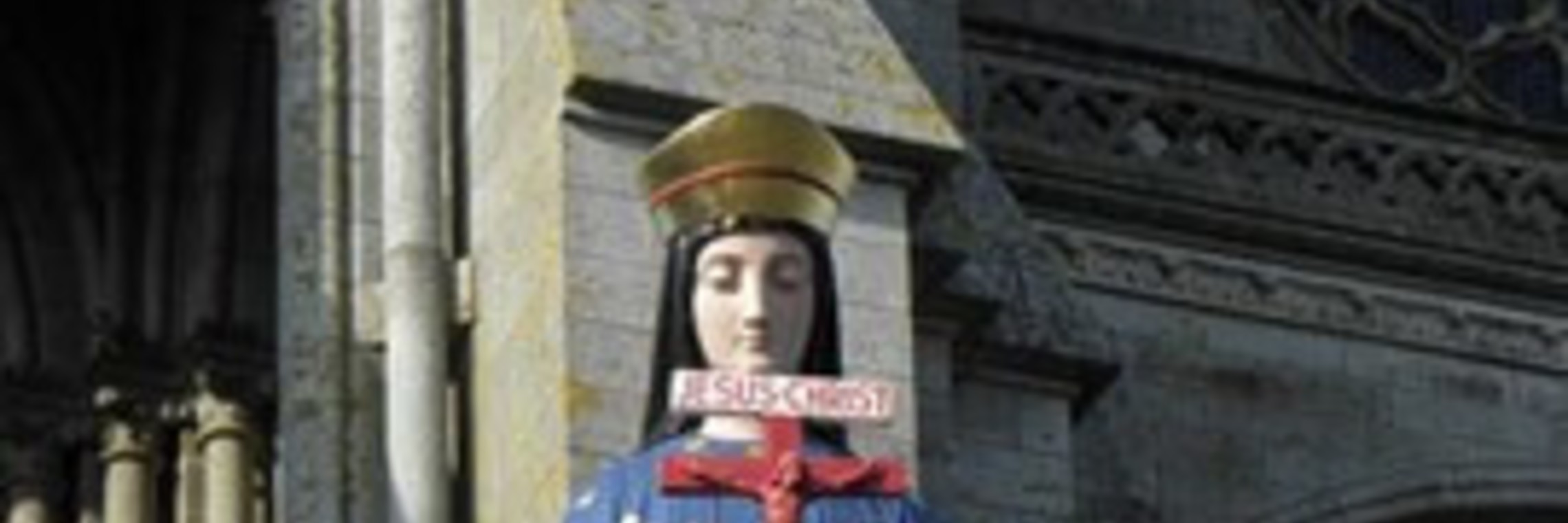a statue of the Marian apparition in Pontmain holds a red crucifix 
