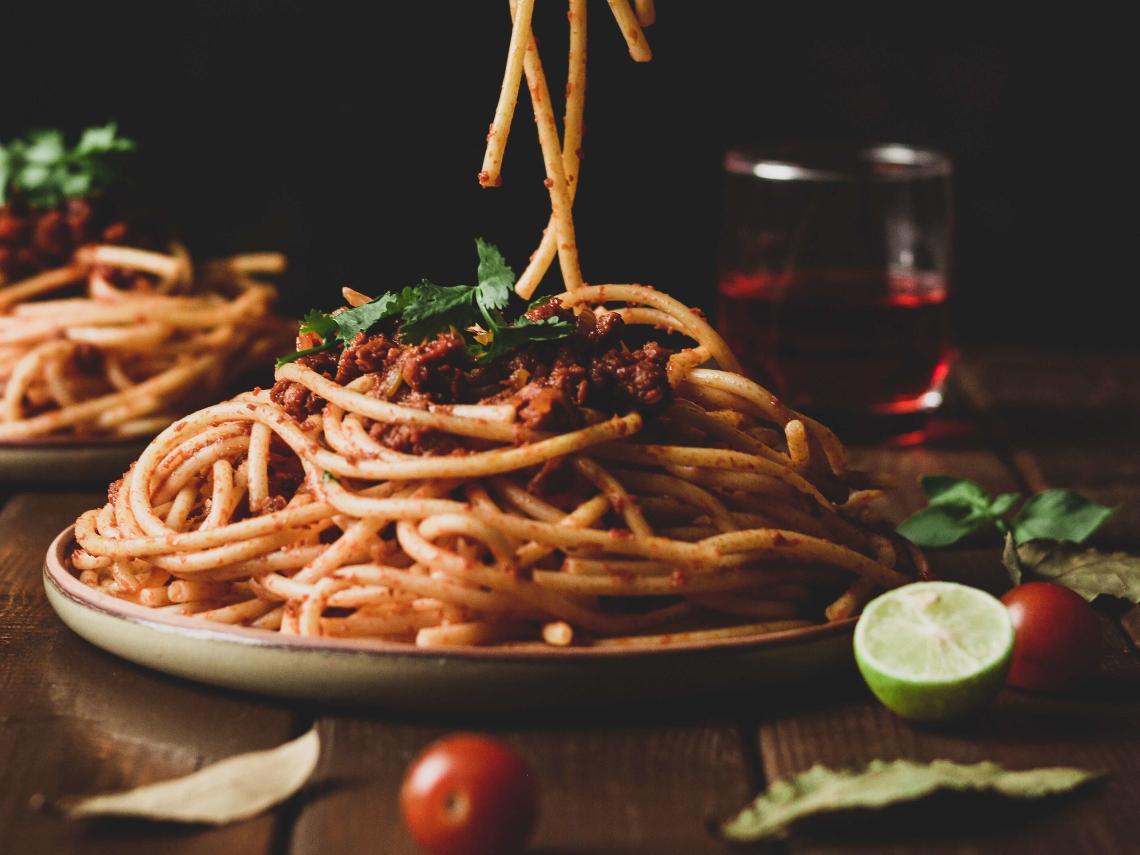 a plate of spaghetti with tomato sauce sits on a wooden table with an unseen person grabbing a forkfull of noodles